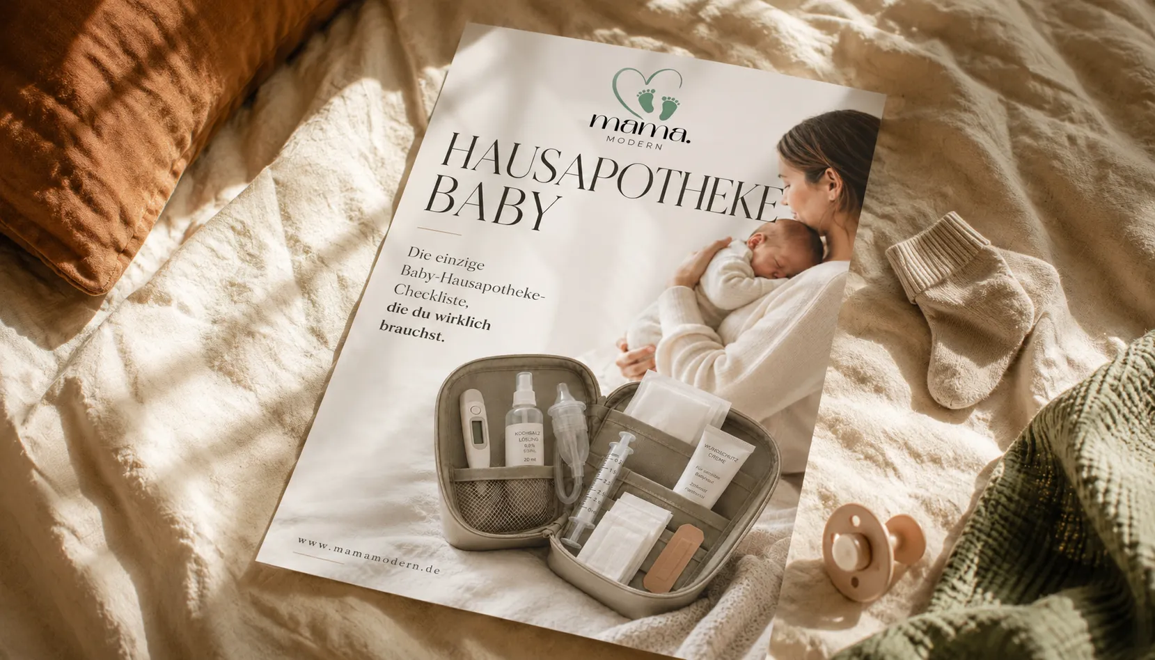 Hausapotheke Baby Checkliste von MamaModern auf cremefarbenem Bettzeug mit Babysöckchen