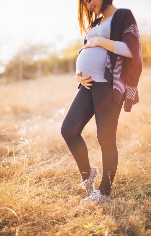 Schwangere Frau im goldenen Gegenlicht hält ihren Bauch, Mama Blog MamaModern